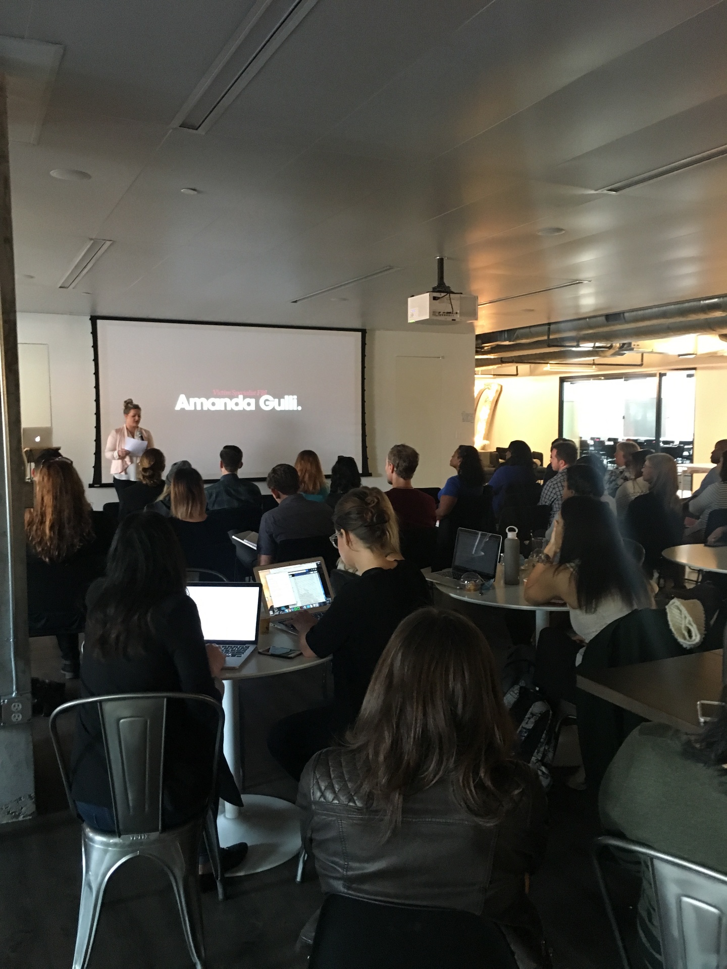 FBI Victim Specialist Amanda Gulli giving a keynote talk to a packed room of Huge employees, with her name projected on screen.
